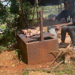 Images of a man cooking a whole goat leg on a large barbecue