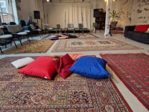 Downstair Studio decorated with a number of rugs and chairs placed in a semi-circle, also with the stage in the background.