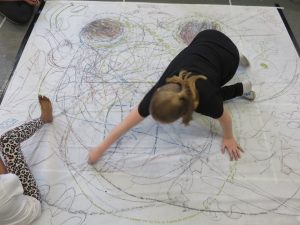 Image of young person from above making marks on a very large piece of paper