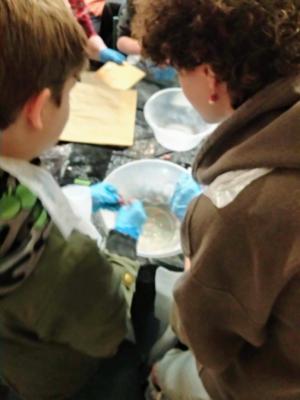 Image of behind of two people with their hands in a plastic bowl. There is flour inside.