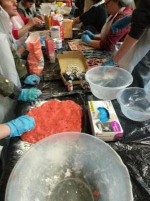 Image along table with lots of people making cookies. Someone has a large piece of pink dough that they are rolling out