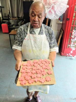 Image of man standing holding a tray of cookies, he is smiling. Behind him, inside the room is a huge paper cherry blossom, next to an old red telephone box.