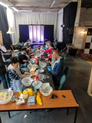 Image of around twenty people along a long table filled with all sorts of sweet and cookie-making tools and ingredients. They seem to be concentrating very hard.